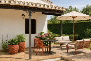 Terraza exterior de estilo mediterráneo con sillas terracota, conjunto de sofá y sillones de jardín, sombrilla beige y maceteros decorativos.